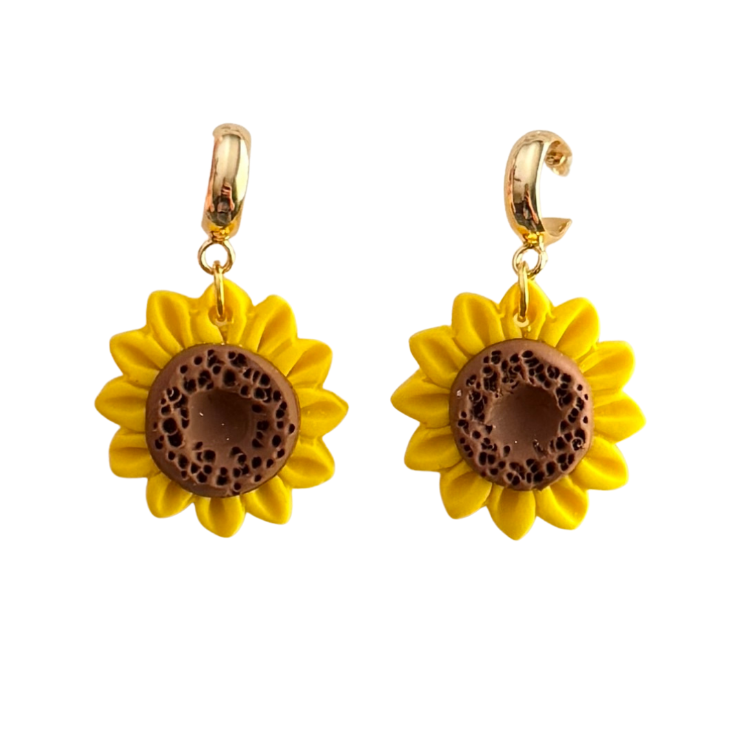 Handmade yellow and brown sunflower polymer clay earrings hanging from gold huggie cuffs